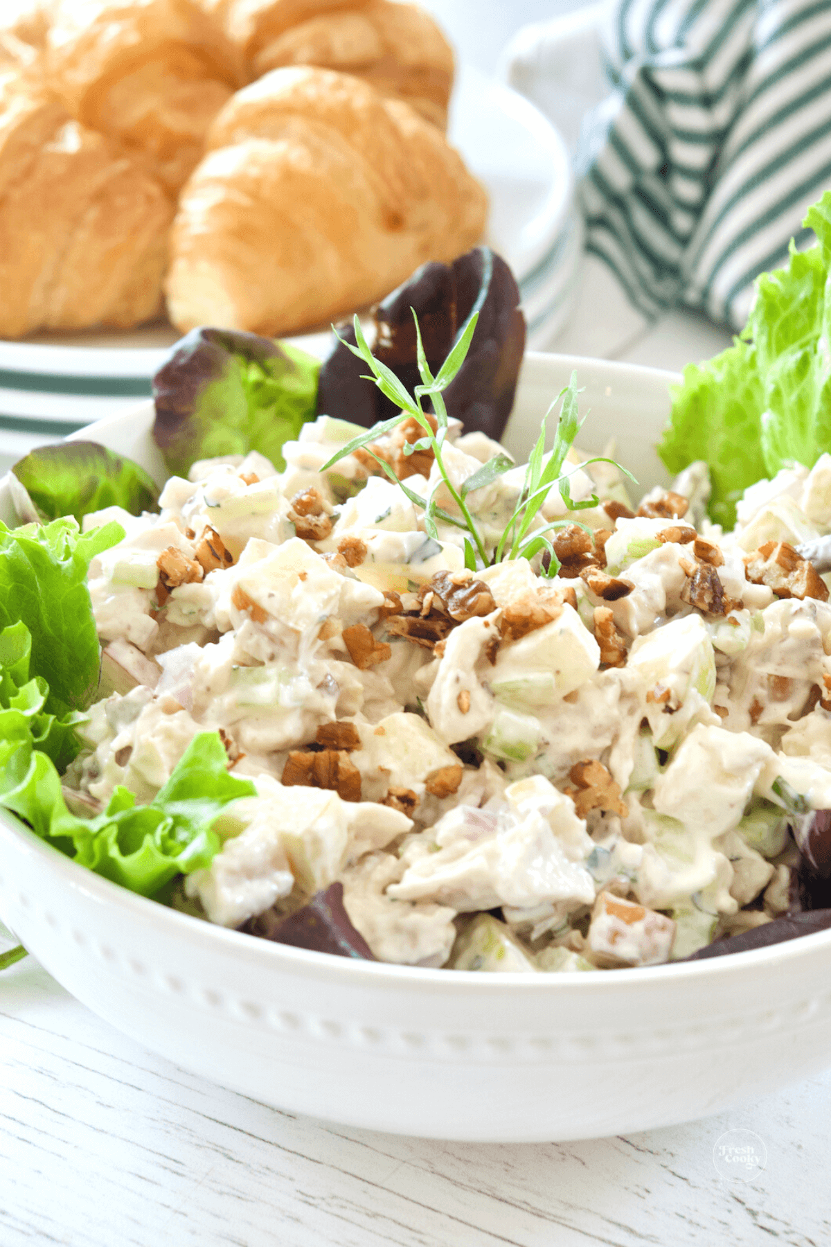 Bowl filled with apple pecan chicken salad with tarragon, croissants behind.