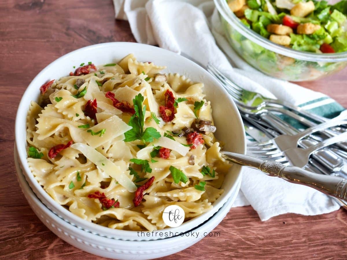 Creamy Bow Tie Pasta with Sun-dried tomatoes in large pasta bowl with salad in background.