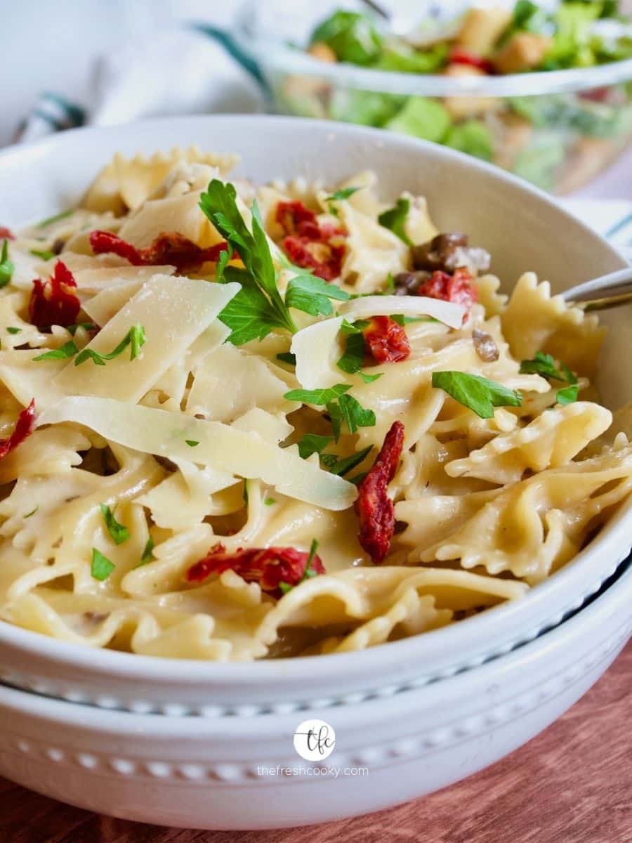 Creamy bow tie pasta in a large bowl with sun-dried tomatoes, basil, all made in your instant pot!