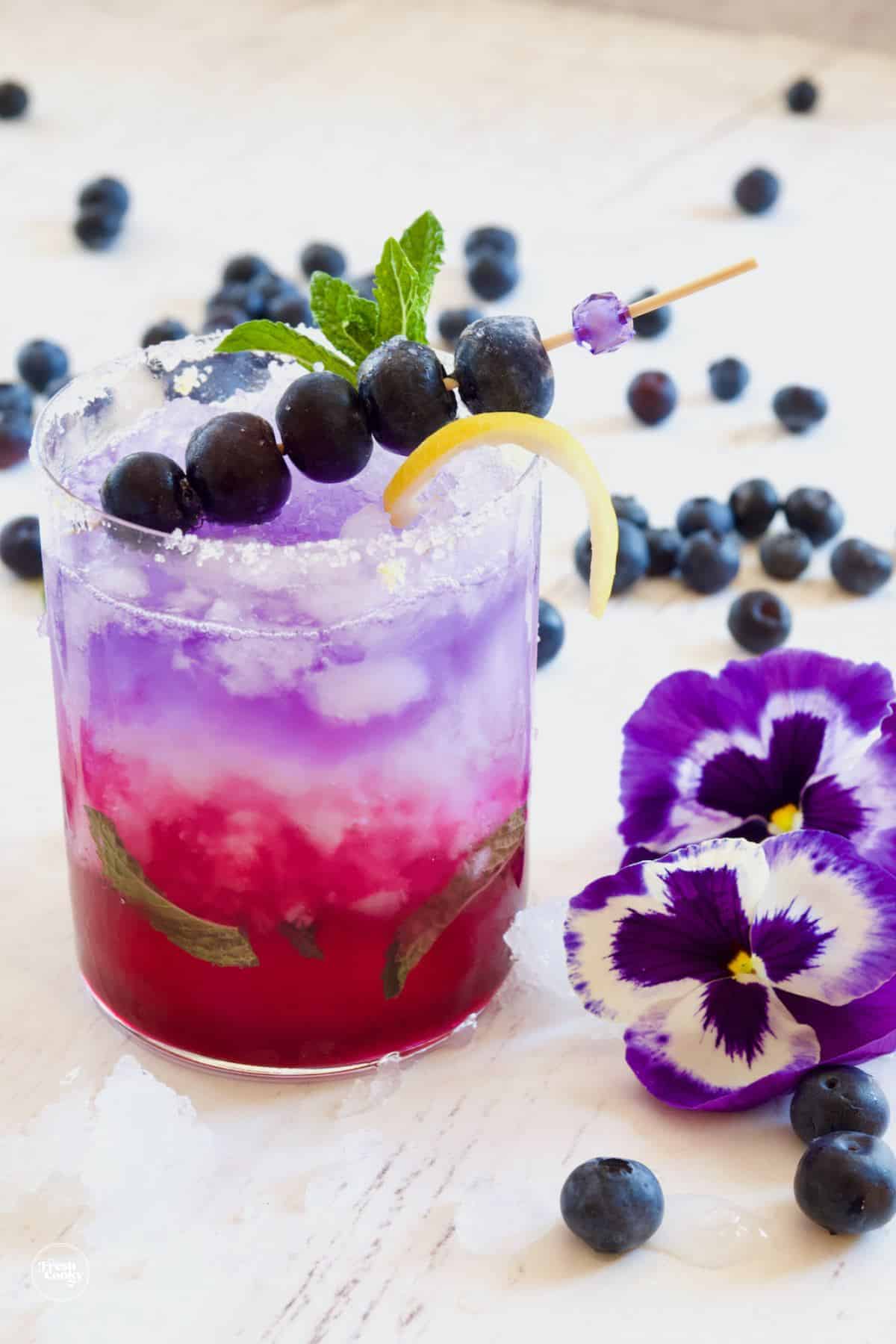A layered cocktail with red white and blue coloring, using blueberry syrup, ginger beer and Empress gin.
