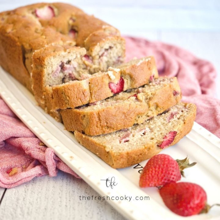 Horizontal image of sliced fresh strawberry bread on pretty platter with fresh strawberries.