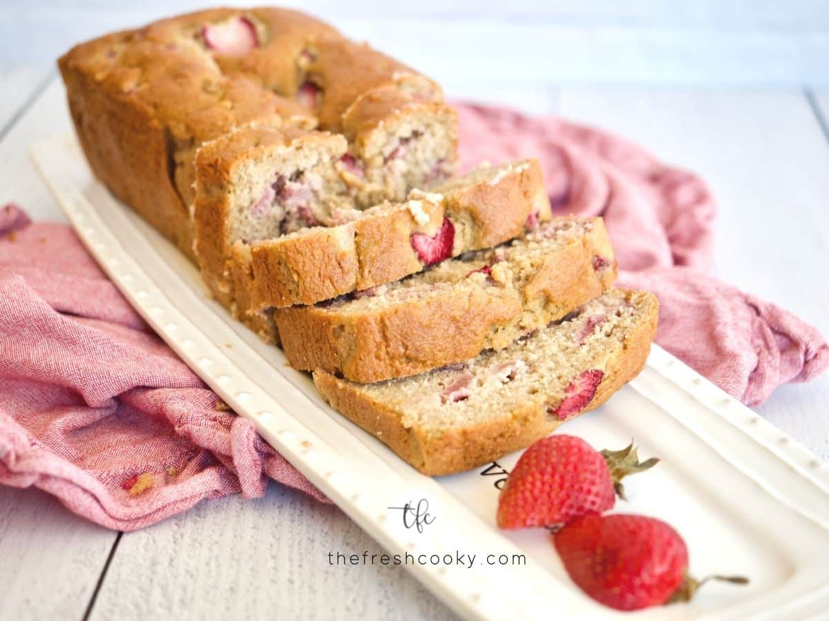 Horizontal image of sliced fresh strawberry bread on pretty platter with fresh strawberries.