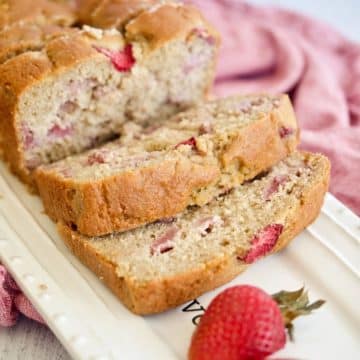 Sliced loaf of strawberry bread on pretty platter with fresh strawberries.