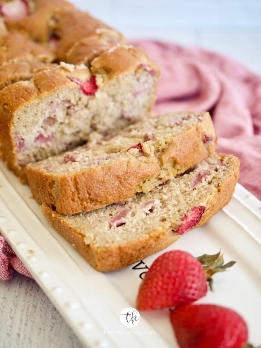 Sliced loaf of strawberry bread on pretty platter with fresh strawberries.