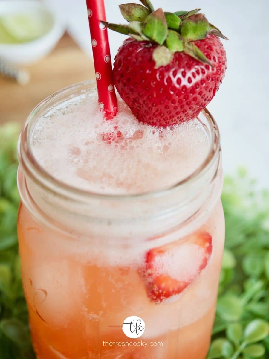 Strawberry refresher drink close up, with strawberry on edge of glass with straw.