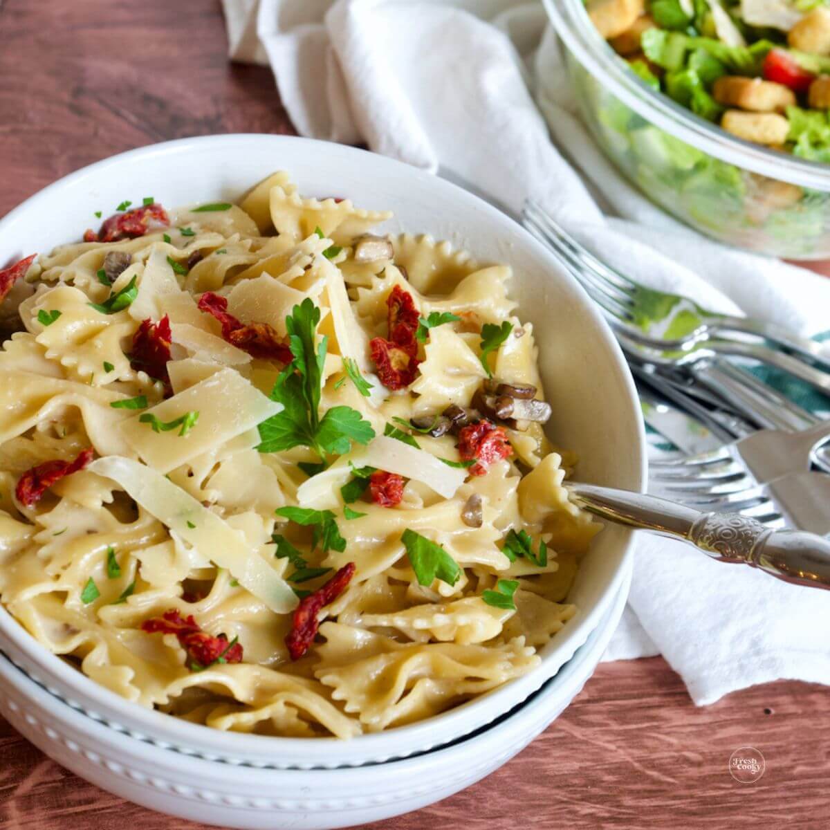 Creamy bow-tie pasta in pasta bowls with Italian salad behind.