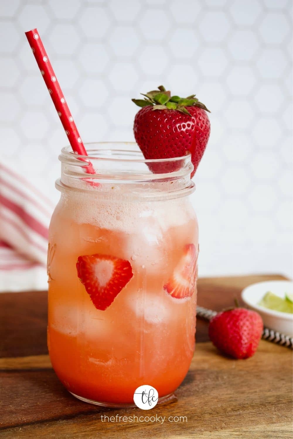 Delicious Strawberry Refresher on cutting board with strawberries and a lime and a pretty straw.