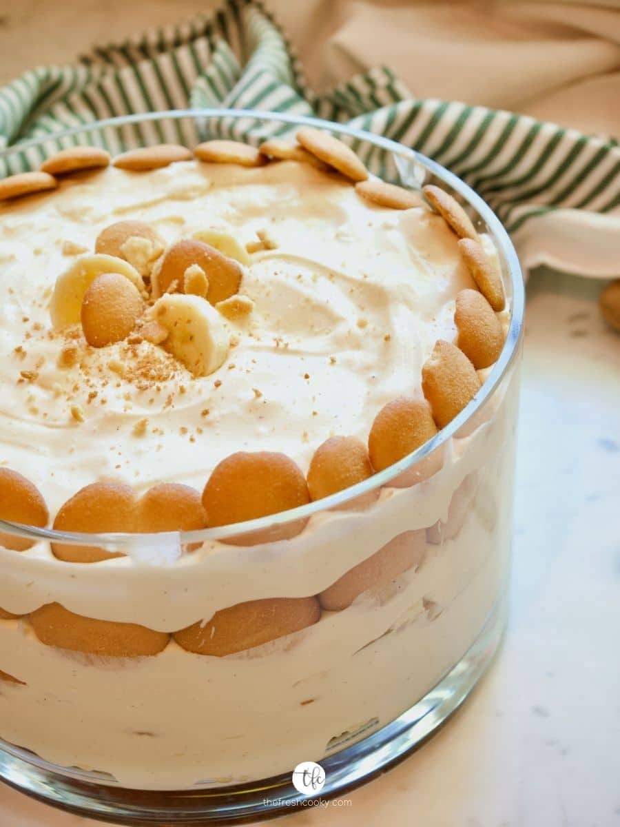 Large glass bowl filled with Magnolia Banana Pudding with a green and white striped towel in background.