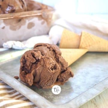 Image of scoop of dark chocolate ice cream with brownie bits in a sugar cone laying on a galvanized tray.
