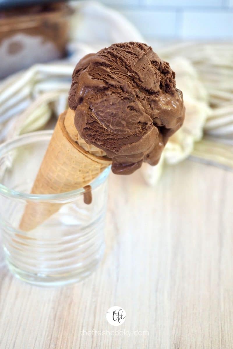 Scoop of Chocolate Brownie Ice Cream in sugar cone in a glass with a drip on the side.