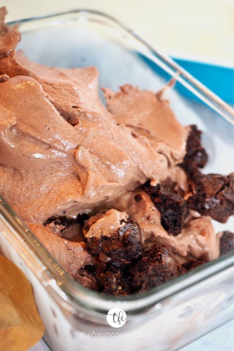 Process shot of combining chocolate ice cream and fudge brownie bites into storage container.