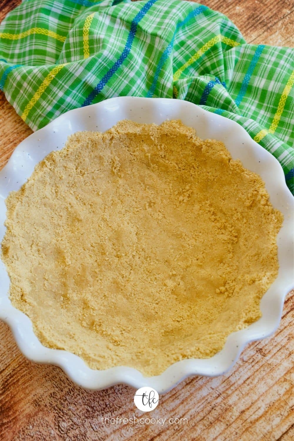 Perfect Golden Oreo Cookie Pie Crust in a white ruffled edge deep pie plate with a green plaid towel behind.