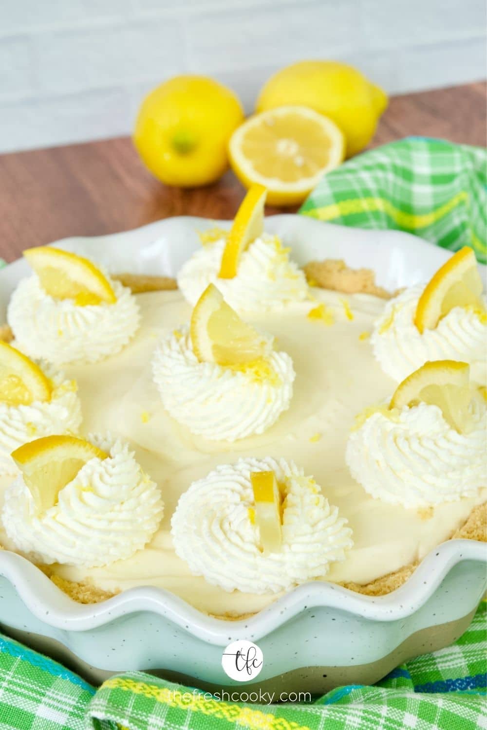 Lemon Cream pie with swirls of whipping cream, topped with lemon wedges and lemon zest.