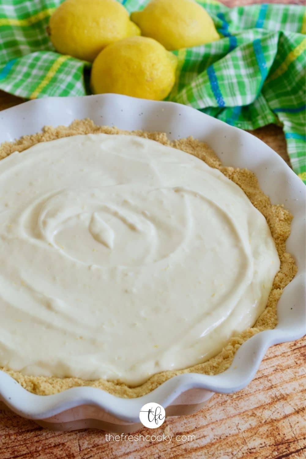 Plain Lemon Cream Pie in a pretty ruffled pie dish with lemons and a green plaid towel behind.