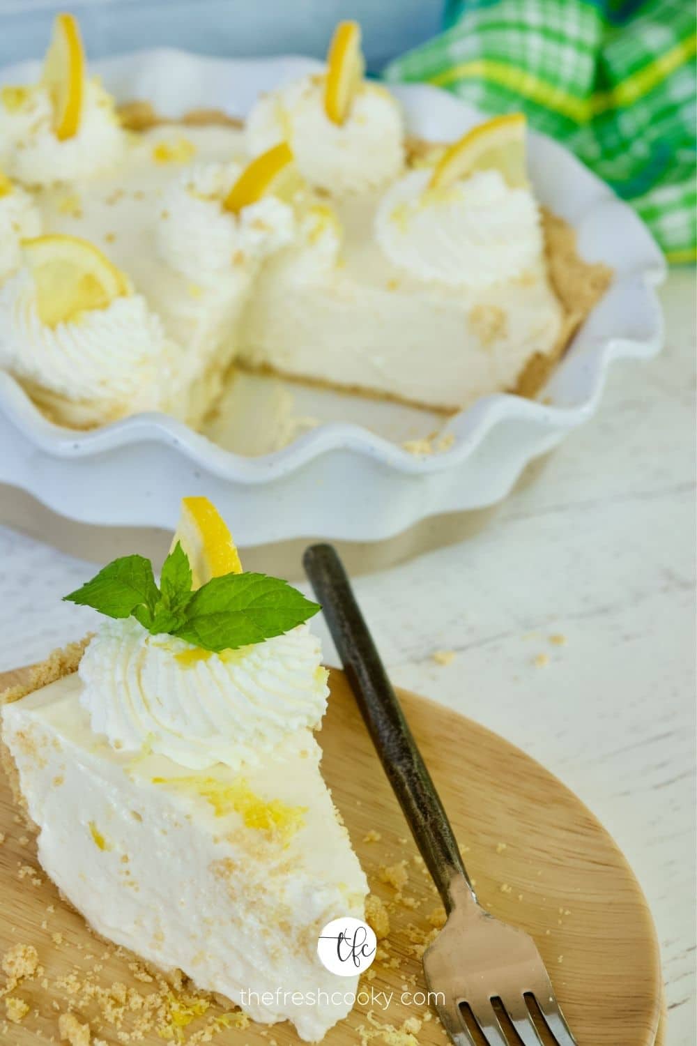 Lemon Cream Pie with slice on plate decorated with lemon zest, whipped cream and mint.