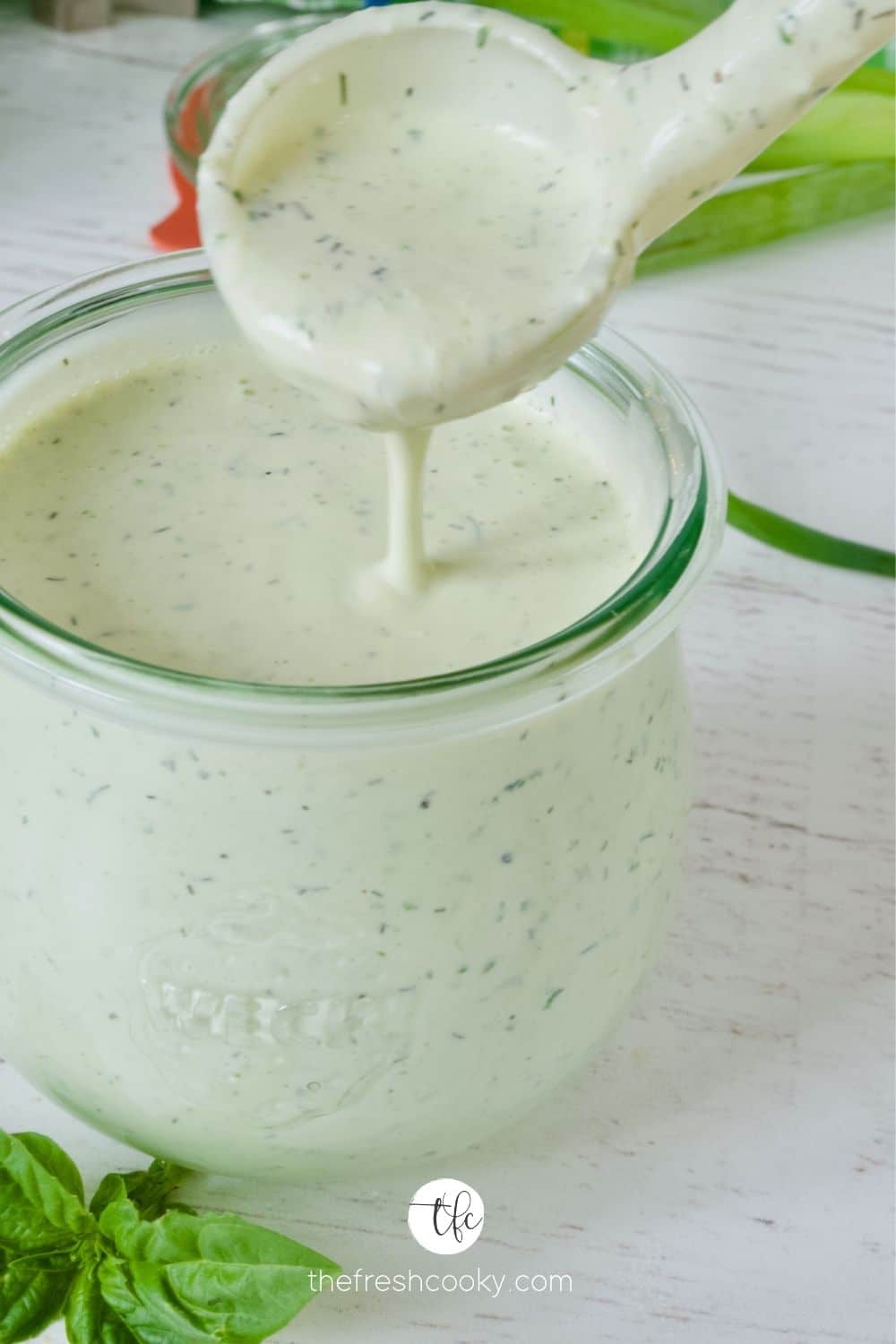 Creamy Buttermilk Ranch Dressing in a Weck tulip shaped jar with spoon pouring some ranch dressing into the jar.