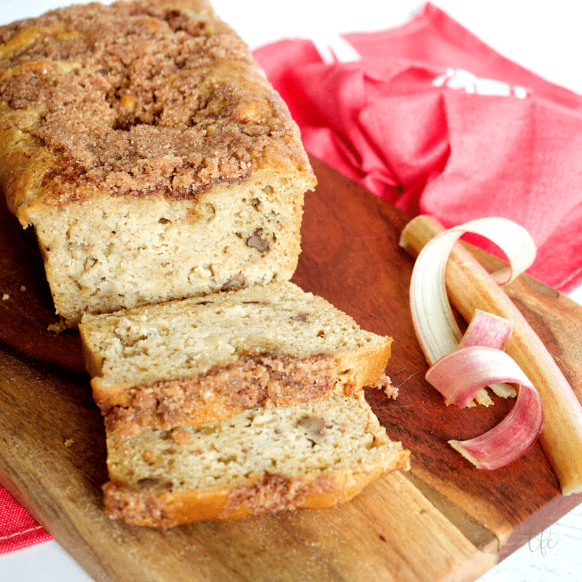 Buttermilk rhubarb bread on cutting board sliced with ribbons of rhubarb net to the bread.