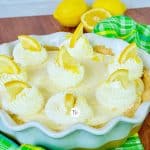 A full size Lemon Cream Pie square shot with wedges of lemon on top of dollops of whipped cream.