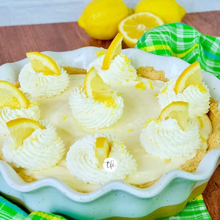 A full size Lemon Cream Pie square shot with wedges of lemon on top of dollops of whipped cream.