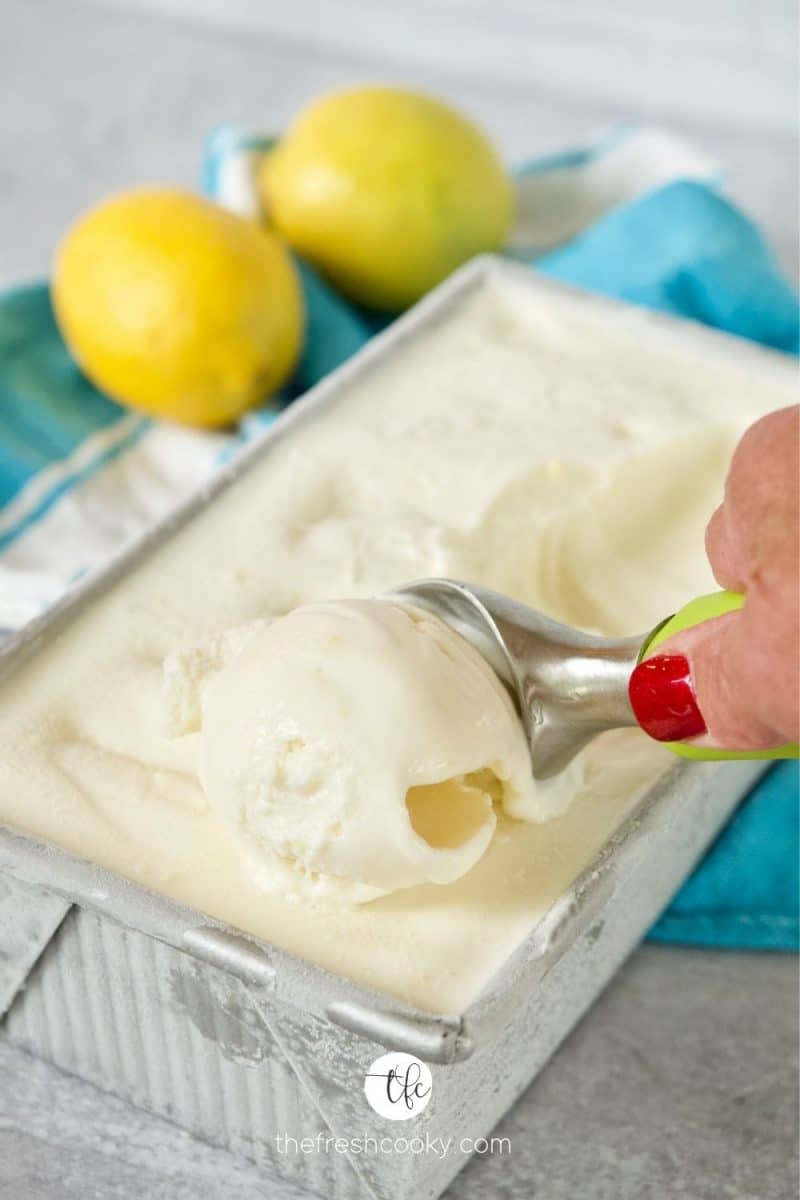 Hand scooping delicious Lemon Ice Cream Lemon Gelato out of a loaf pan with lemons in the background.