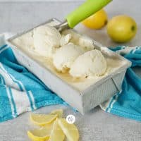 Square image of lemon gelato ice cream with three scoops in pan and an ice cream scoop with lemon slices in front and whole lemons behind.