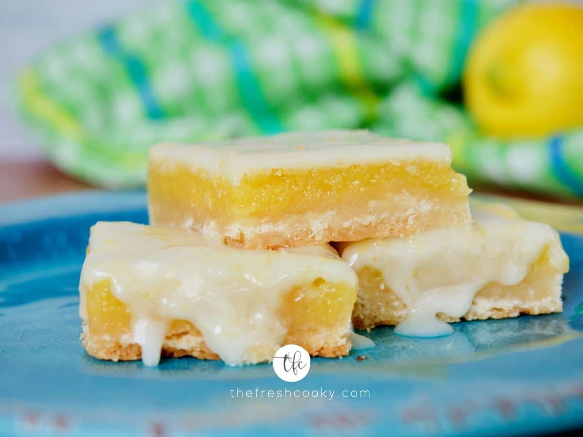 Facebook image of three stacked gooey old fashioned lemon squares with drippy glaze on top.