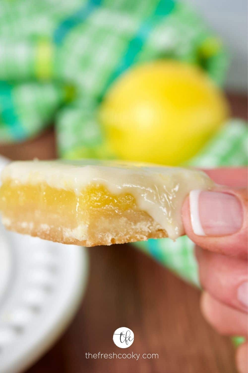 Hand holding an old fashioned lemon square dripping with fresh lemon glaze.