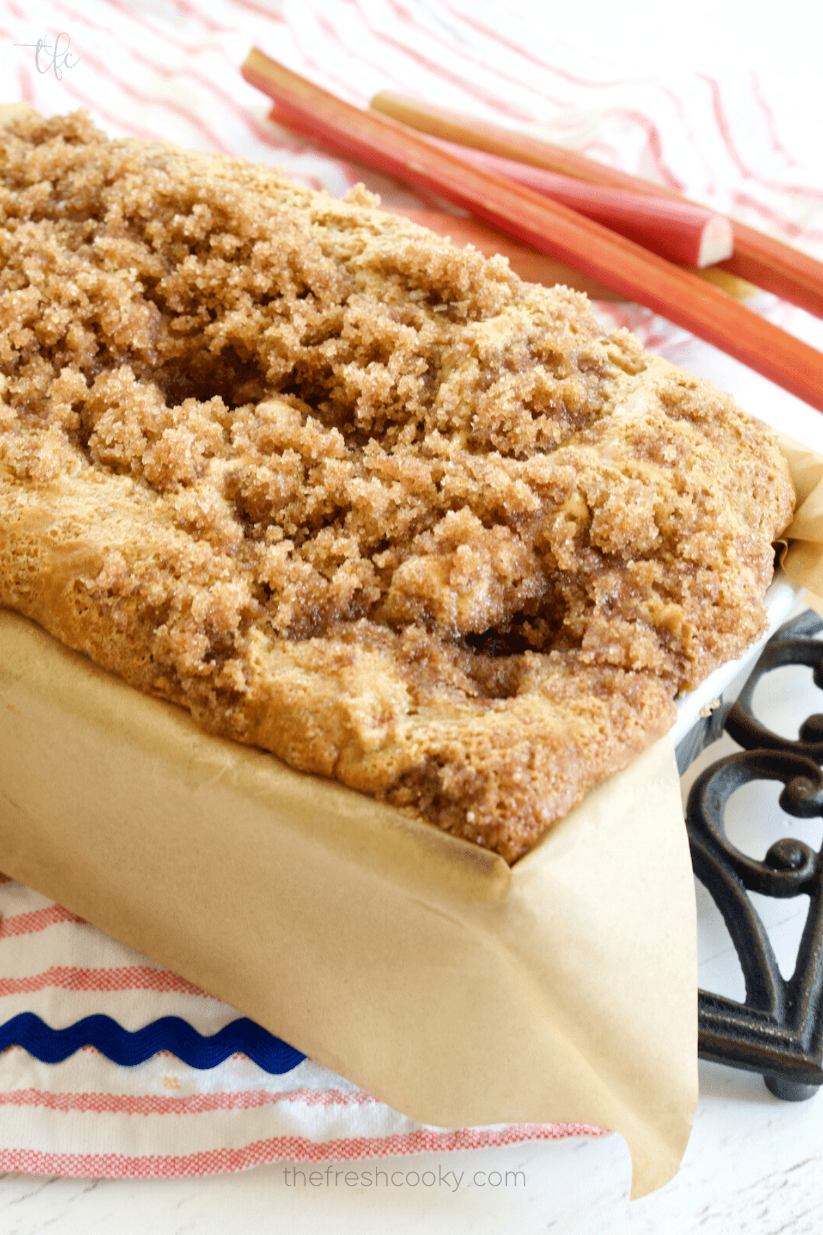 Loaf of cinnamon streusel topping buttermilk rhubarb bread in loaf pan lined with parchment paper.