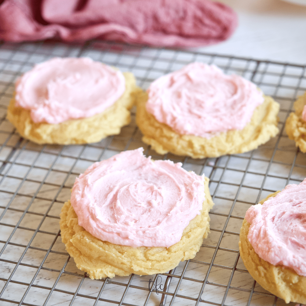 Soft Chewy Crumbl Sugar Cookies on wire rack with pink sweet almond frosting.