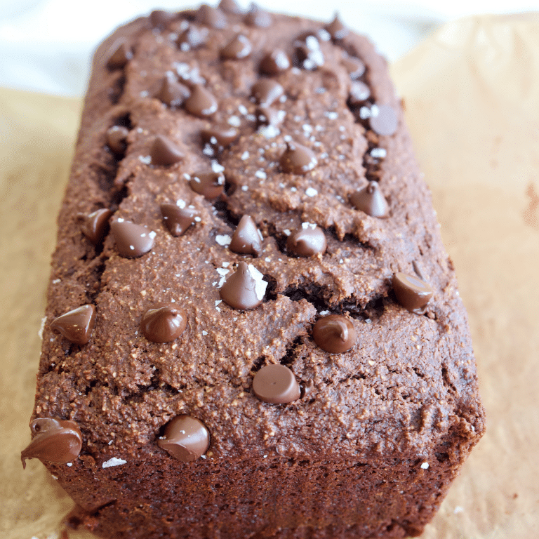 Loaf of healthy chocolate chip banana bread in parchment paper on cooling rack.