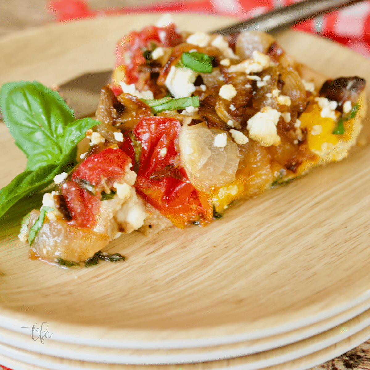 Slice of heirloom tomato pie with fresh basil on a plate with a rustic fork.