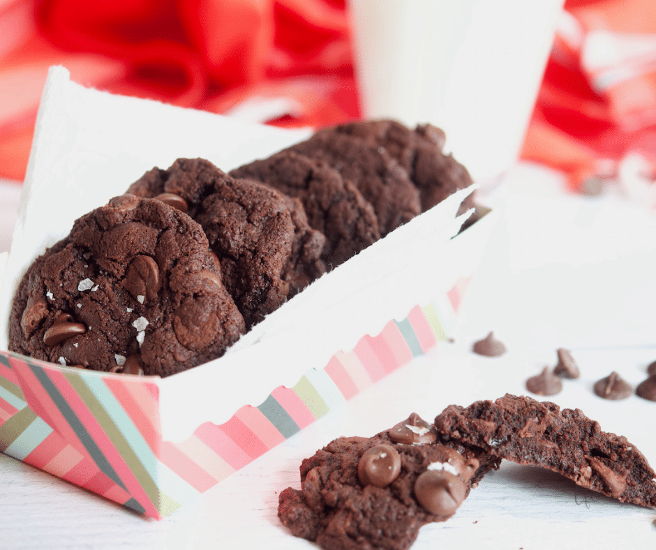 Chewy Triple Chocolate Cookies in a striped box with a cookie broken apart nearby.