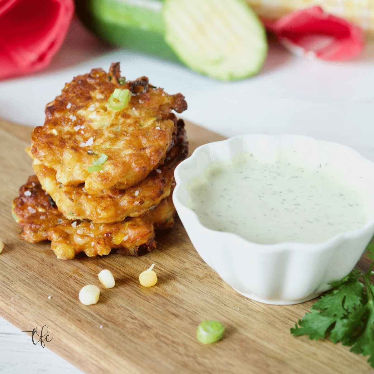 Easy Zucchini Corn Fritters sitting on a cutting board with a small bowl of ranch dressing nearby.