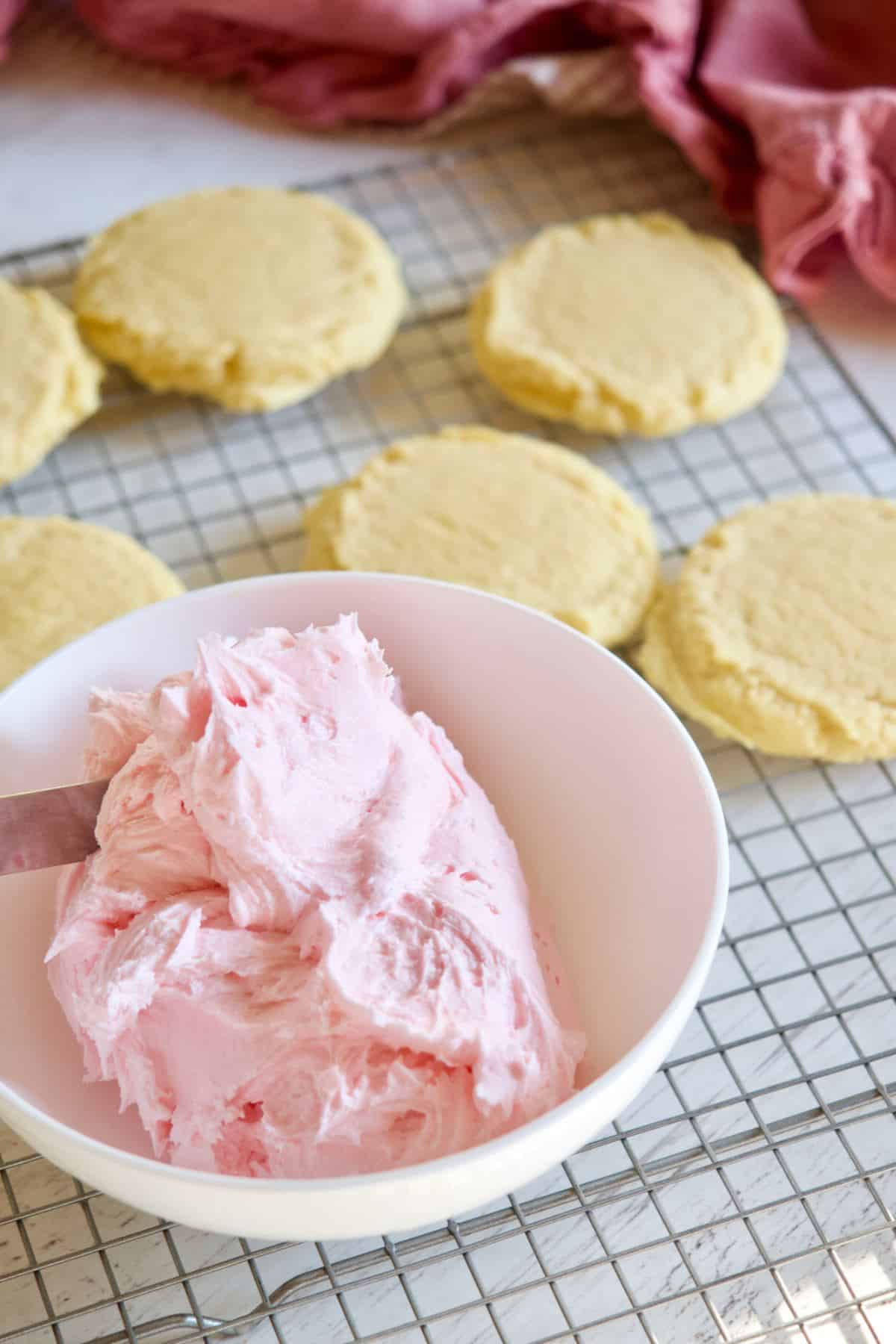 Unfrosted chilled sugar cookies with bowl of pink almond frosting.
