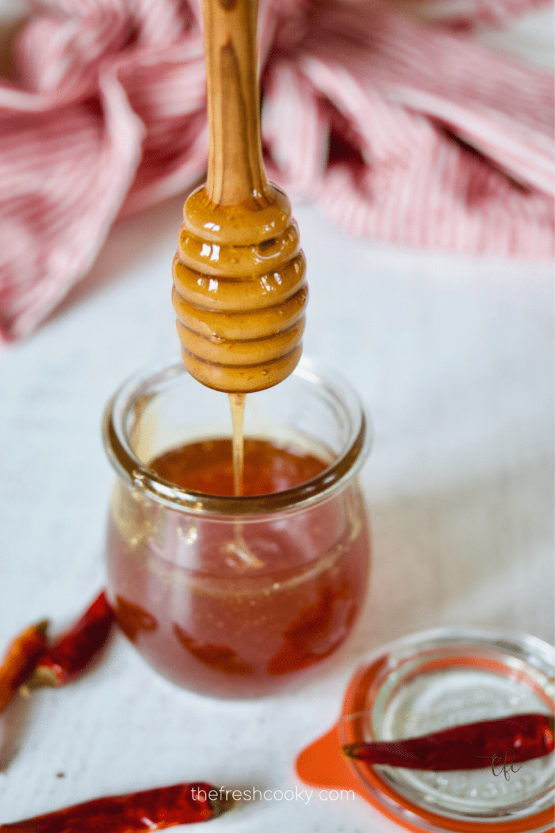 Honey server with honey dripping from it into a jar of hot honey.