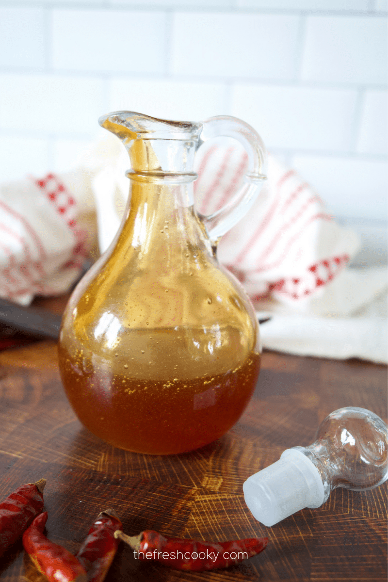 Easy Hot honey in a pretty cruet jar with stopper and chili peppers around.