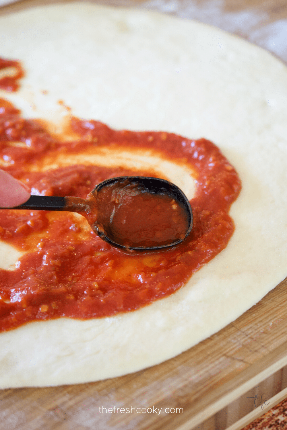 Spreading Best Pizza Sauce on pizza dough.