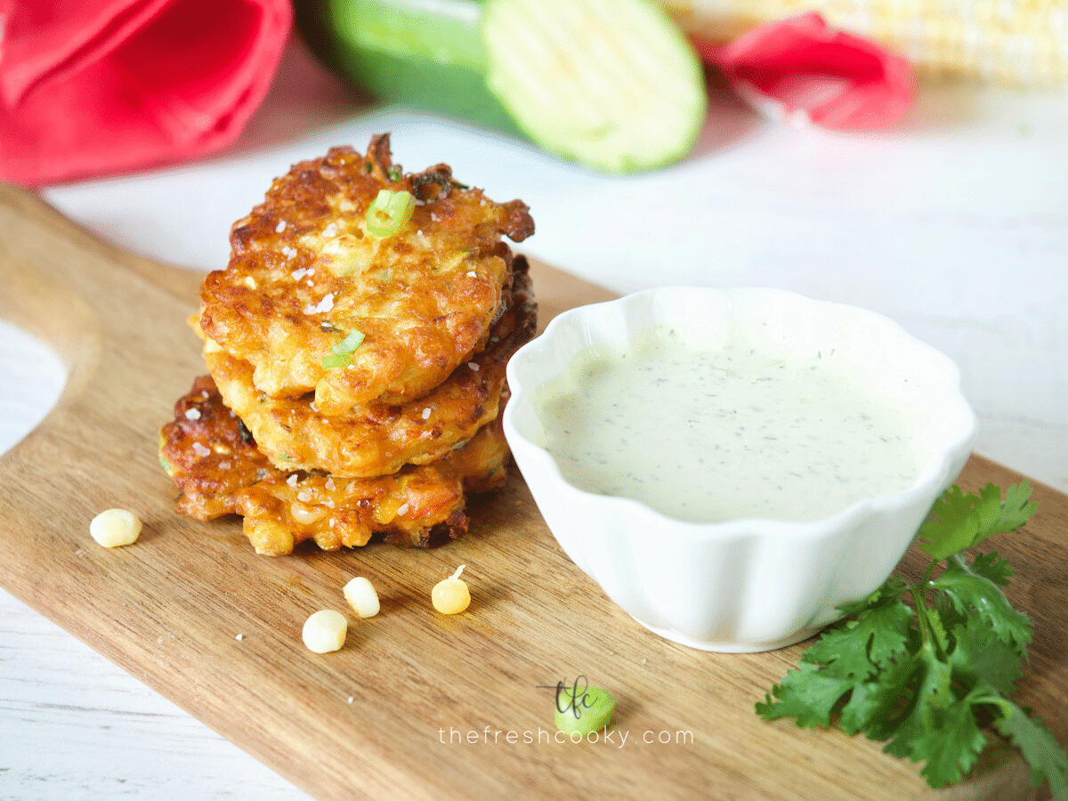 Zucchini Corn Fritters on cutting board with ranch dressing for dipping.