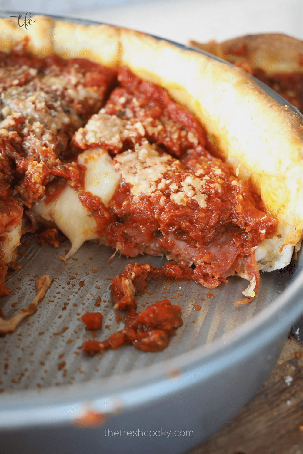 Chicago style deep dish pizza in pan with a slice removed and melting cheese and pepperoni oozing from slice.