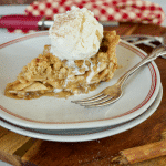 Slice of gluten-free apple pie on a plate with a fork and a scoop of melting vanilla ice cream on top.