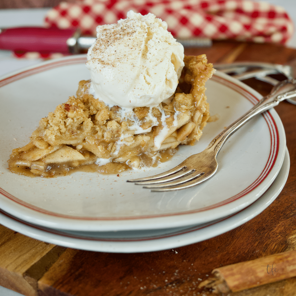 Slice of gluten-free apple pie on a plate with a fork and a scoop of melting vanilla ice cream on top.