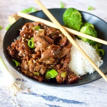 Mongolian Beef image of black bowl filled with Mongolian beef, rice and broccoli with chopsticks on top.
