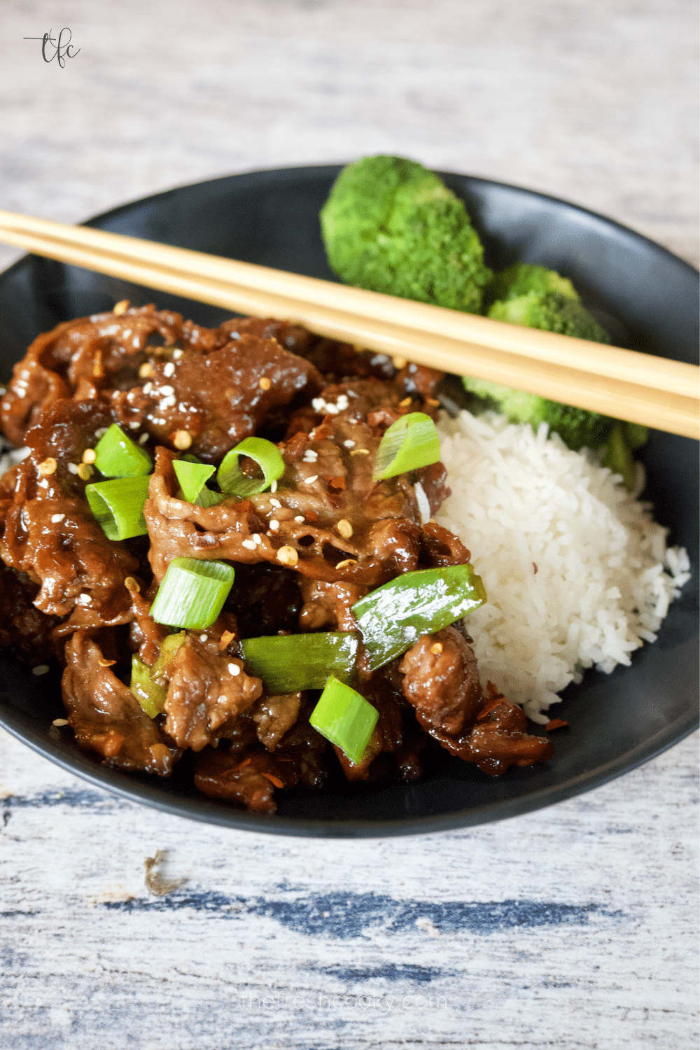 Mongolian Beef crispy and saucy in a black bowl with white rice and steamed broccoli.