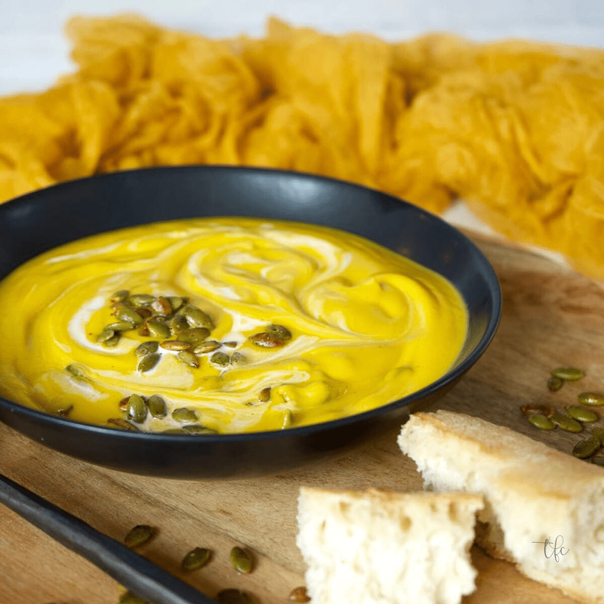 Square image of creamy, silky Panera Autumn Squash Soup with french bread and pepitas.