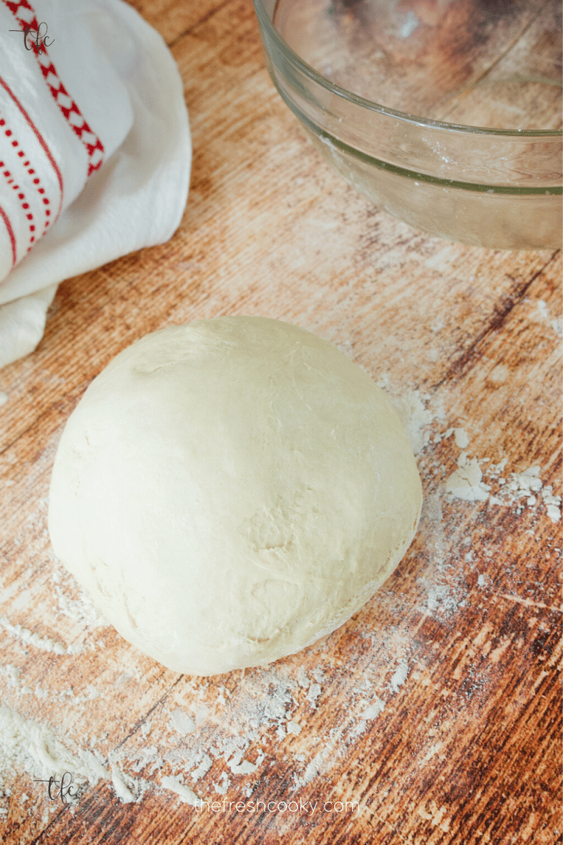 No rise pizza dough on a floured table with a cloth and bowl nearby.