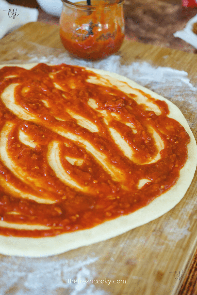 rolled out pizza dough recipe with thick, red, pizza sauce smeared on top.