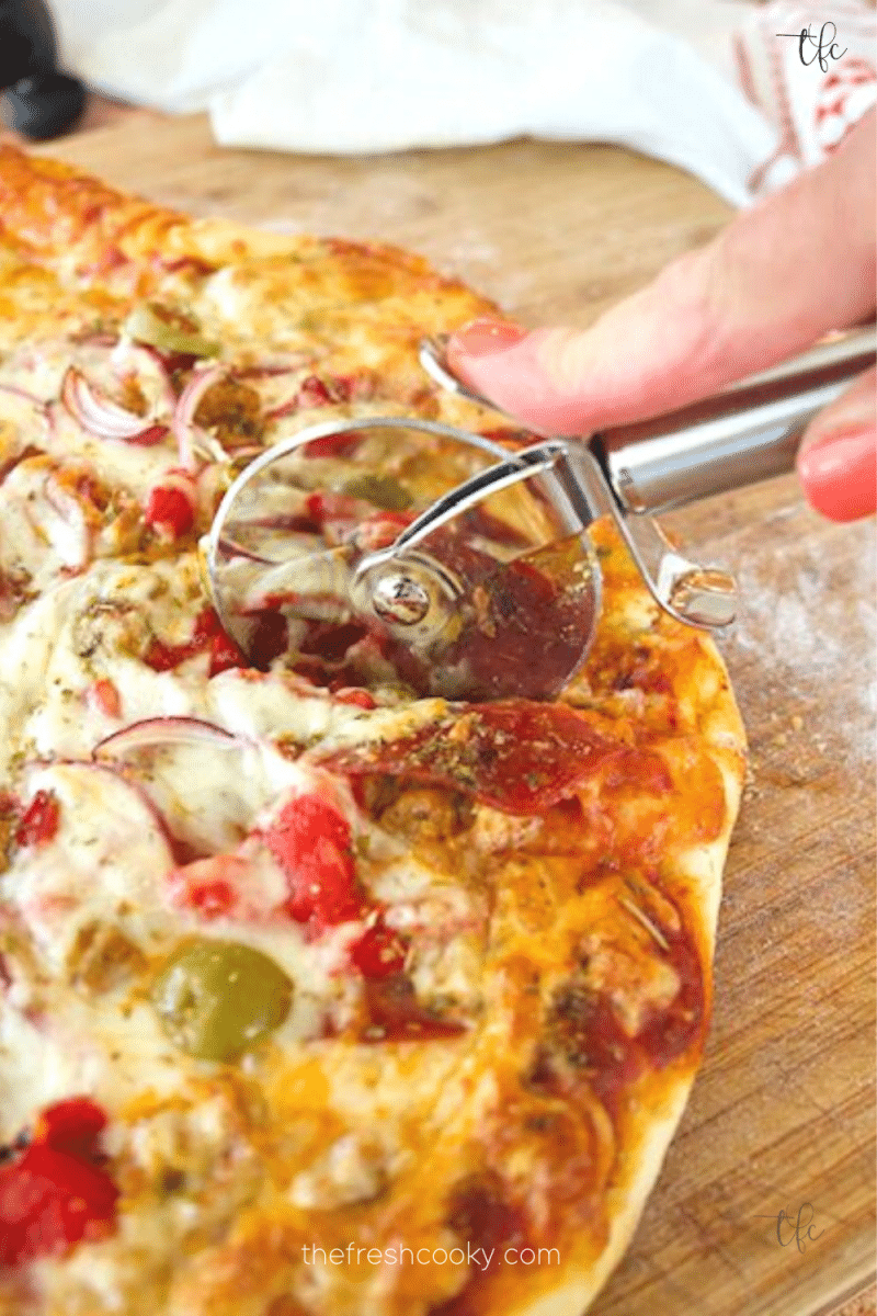 Pizza dough recipe with image of baked pizza and hand using pizza cutter to slice a cheesy piece of pizza.