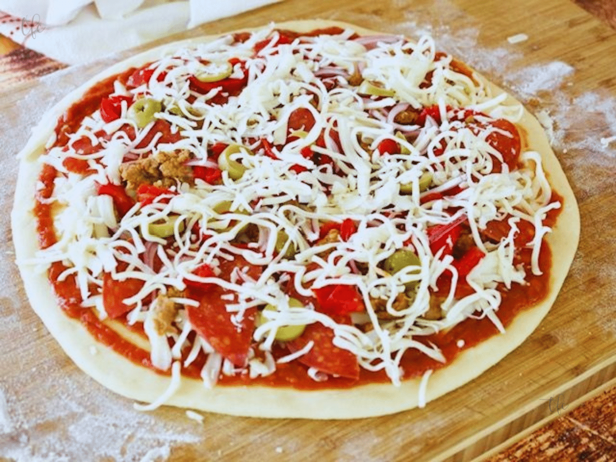 Image of pizza dough rolled out with sauce and toppings on top ready for the oven.