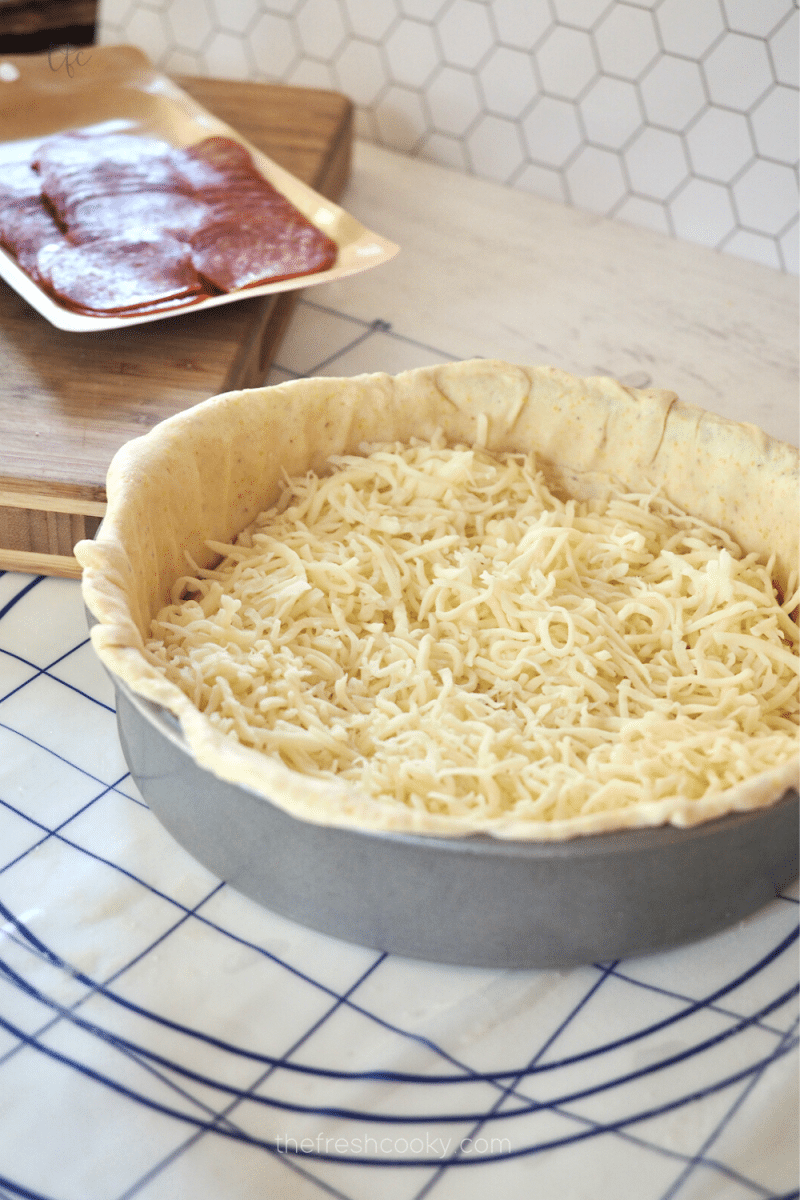 Deep dish pizza dough in pan with mozzarella cheese on bottom.