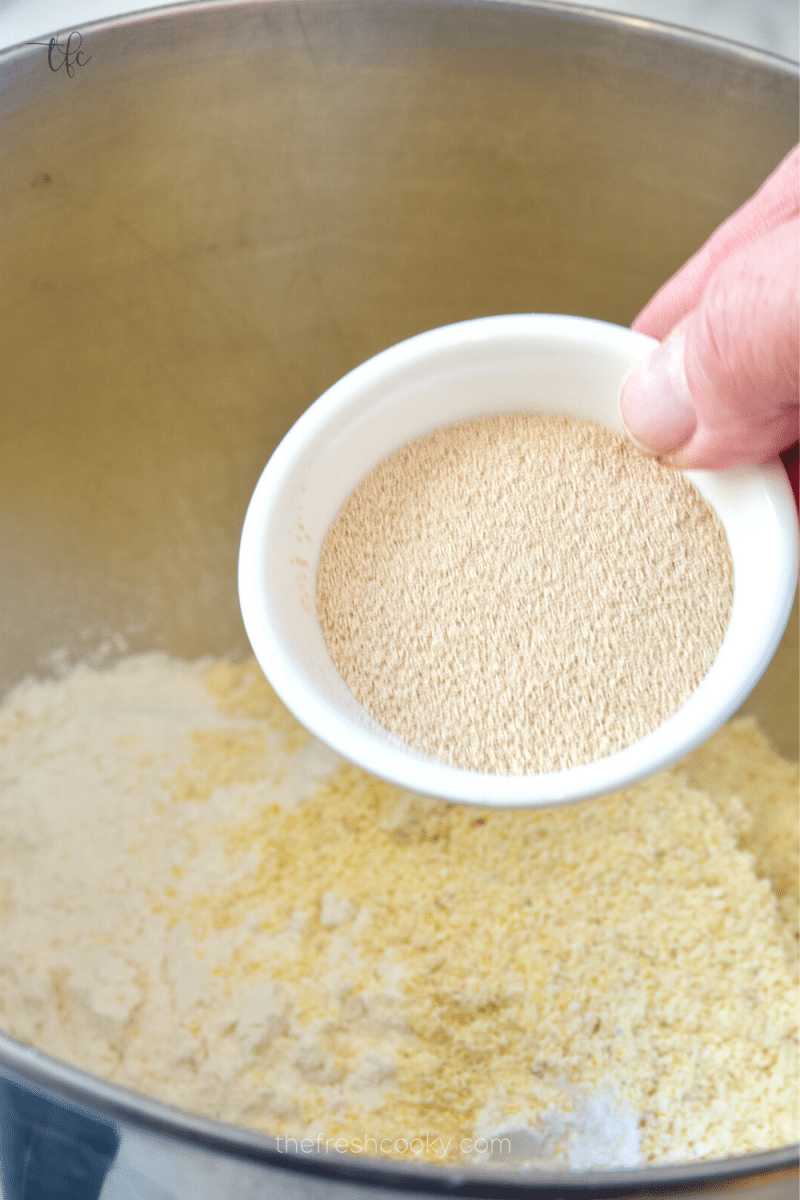 adding yeast and sugar to cornmeal and flour in stand mixer for deep dish pizza dough recipe. 